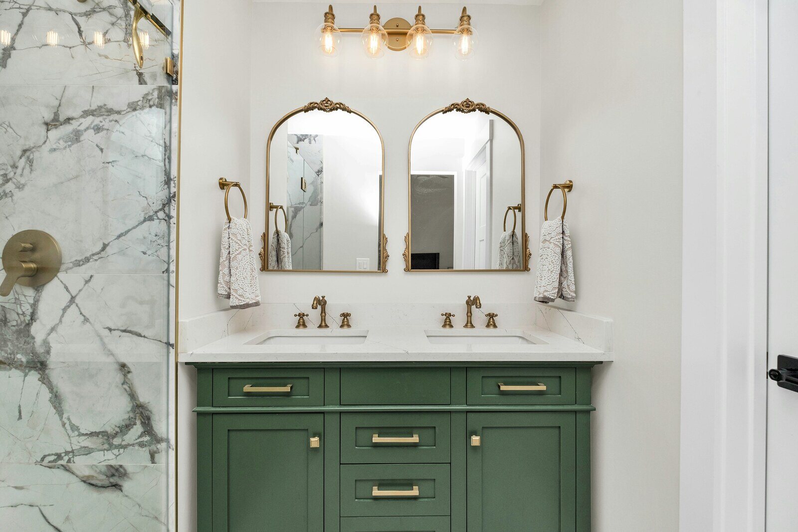 Elegant bathroom remodel featuring a green vanity with gold accents, marble shower, and vintage mirrors by Crosby Home Services in Prescott, AZ