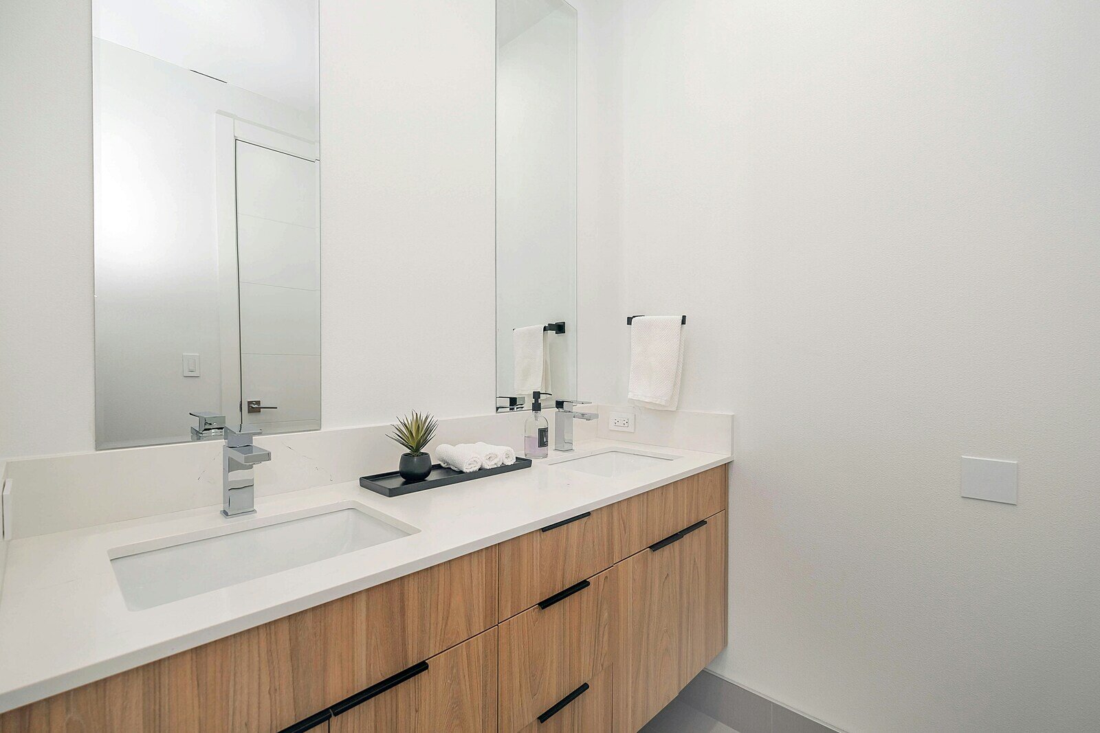 Modern bathroom remodel with a wooden vanity, clean white surfaces, and large mirrors by Crosby Home Services in Prescott, AZ